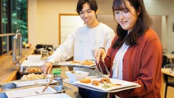 Disposición de un bufé con diferentes alimentos en recipientes metálicos, una persona sirviendo comida y otra sosteniendo una bandeja.