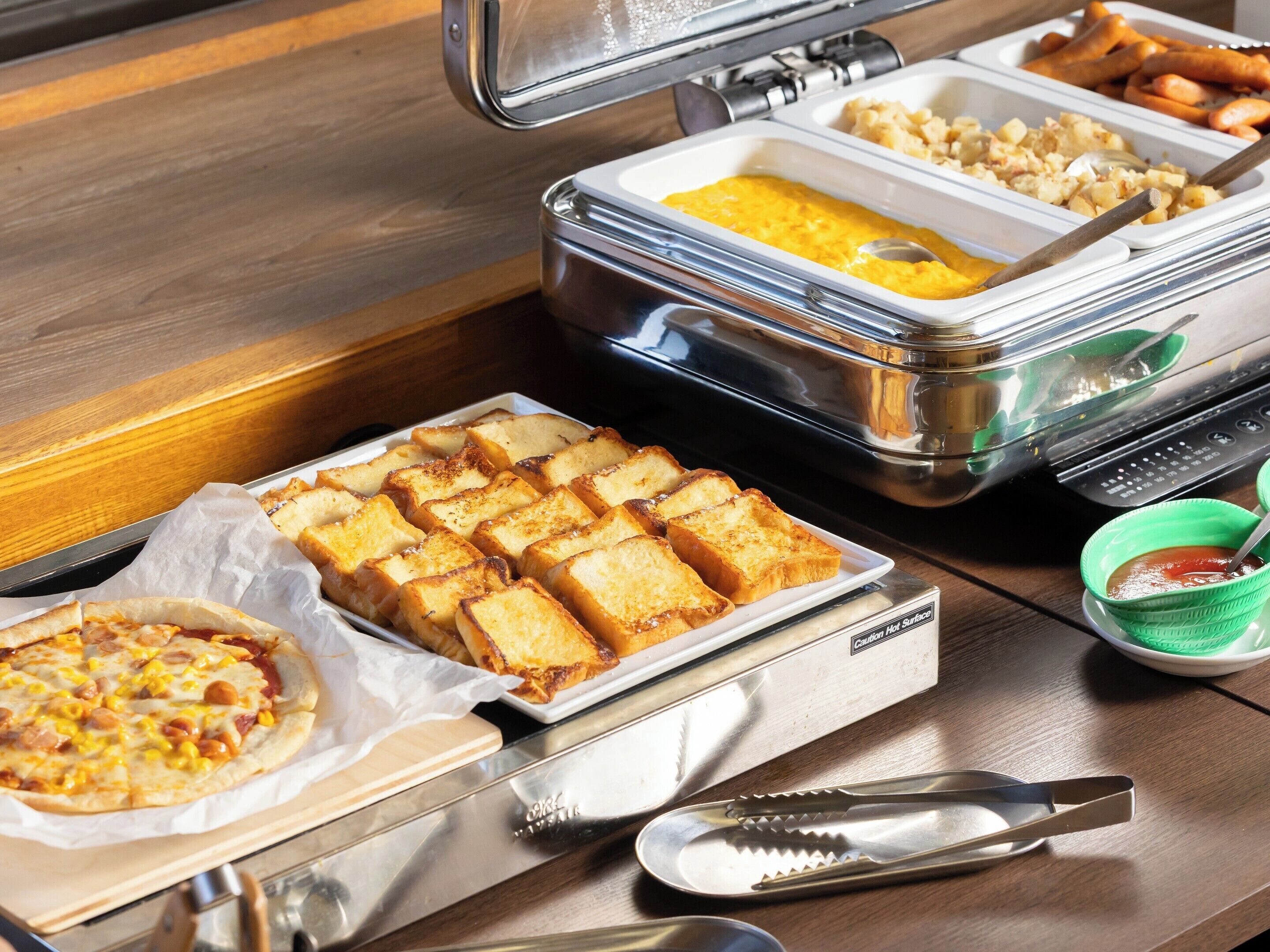 A buffet setup with various food items, including a tray of toast, a container of scrambled eggs, and a bowl of soup.