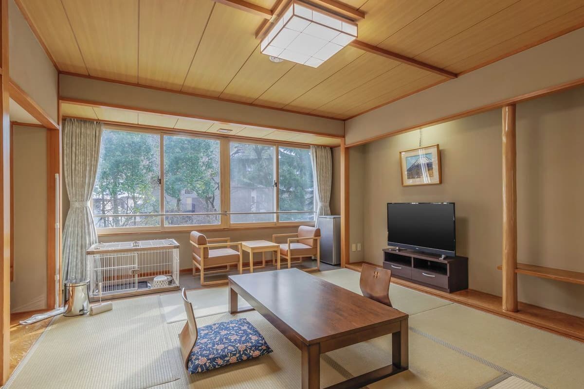 Une pièce de style japonais traditionnel, avec un sol recouvert de tatamis, une petite table en bois, un téléviseur et une vue sur l’extérieur.