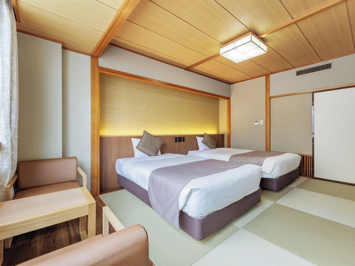 A compact hotel room with two beds, a small seating area, and a kitchenette.