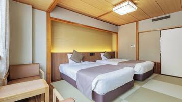 A compact hotel room with two beds, a small seating area, and a kitchenette.