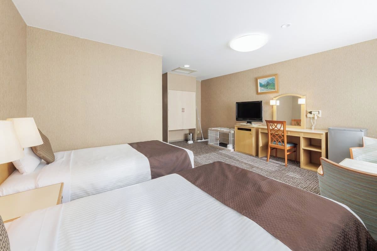 Une chambre d’hôtel avec deux lits, un bureau, une chaise, une télévision et un petit placard.