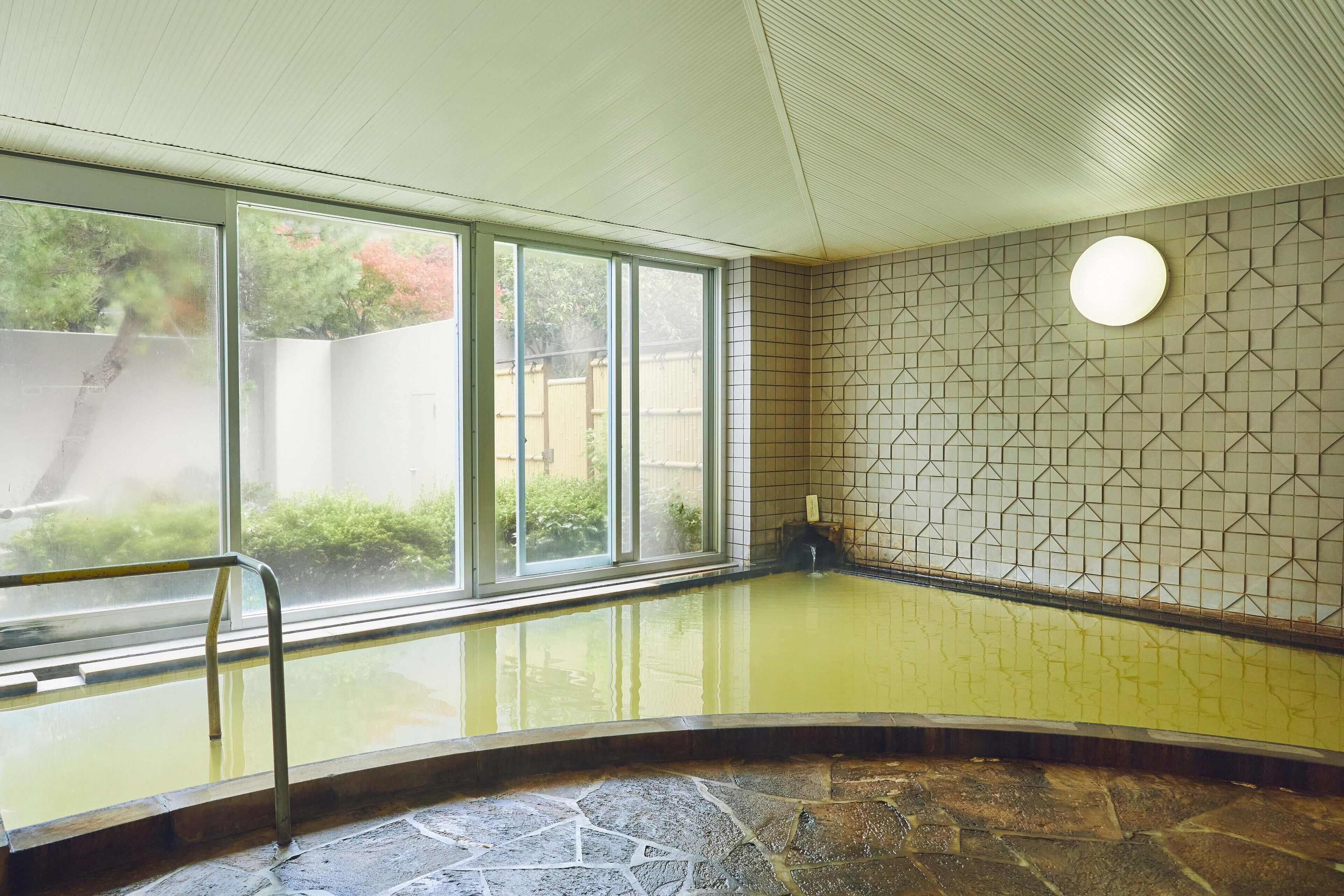 A spa area with a glass-enclosed hot tub, stone flooring, and a tiled wall with a geometric pattern.