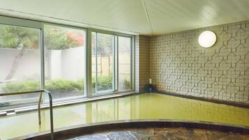 A spa area with a glass-enclosed hot tub, stone flooring, and a tiled wall with a geometric pattern.