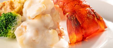 A lobster tail with a creamy sauce, a piece of broccoli, and a side of mashed potatoes on a white plate.