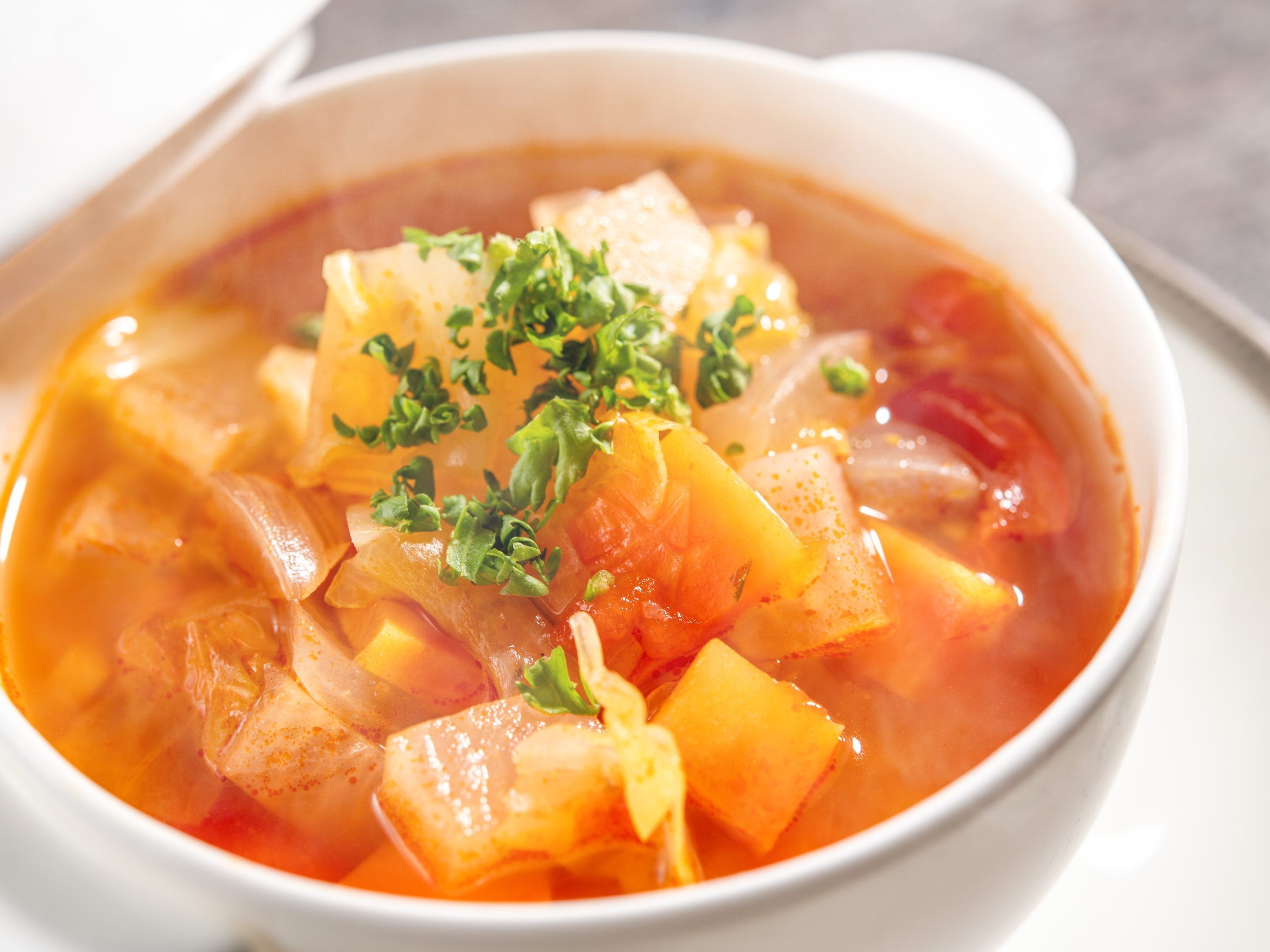 A bowl of soup with vegetables and herbs.