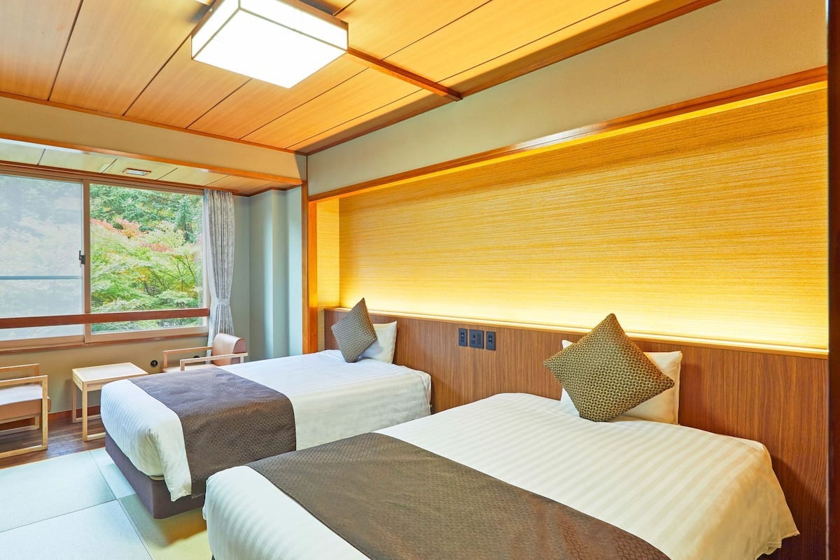 Une chambre avec deux lits, un bureau et une grande fenêtre donnant sur un paysage verdoyant.