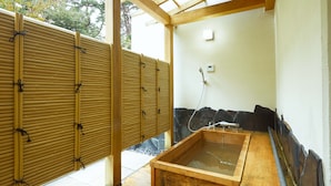 Ein traditionelles japanisches Onsen mit einer hölzernen Quelle, einem Bambusbildschirm und einer Steinwand.