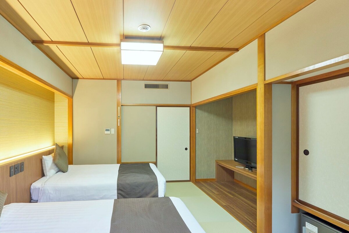 Quarto de hotel com duas camas, uma televisão e um guarda-roupa.