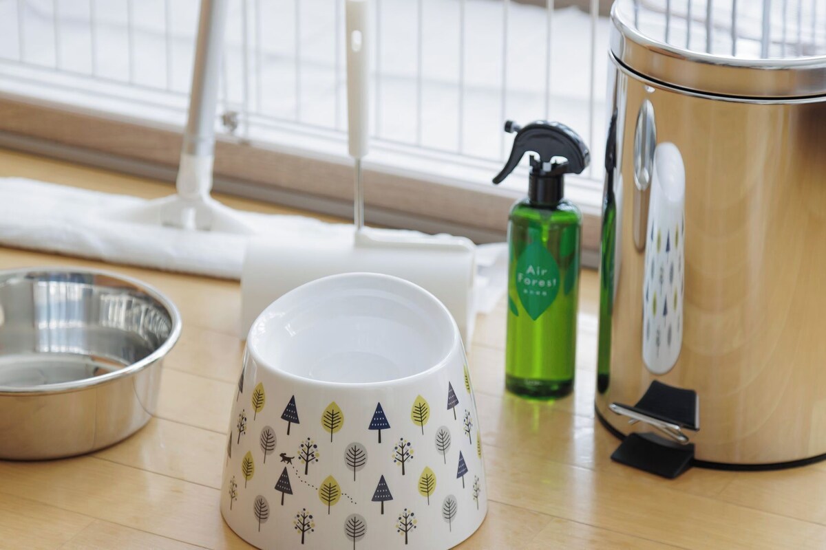 Uma área de cozinha com uma tigela de aço inoxidável, uma caneca branca com desenhos de árvores, um borrifador verde e um eletrodoméstico de aço inoxidável.