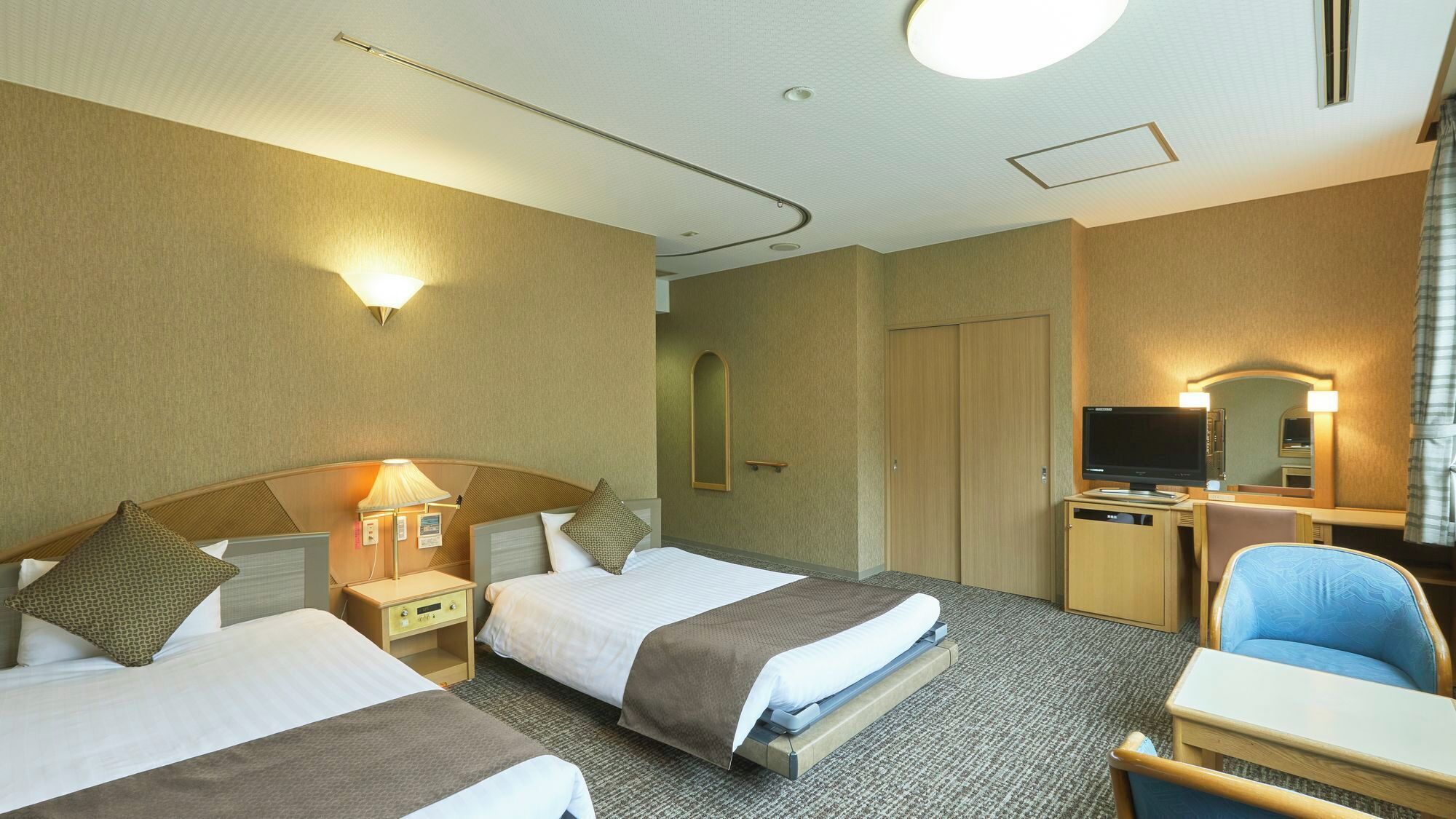 Habitación de hotel con dos camas, un escritorio con ordenador, una silla, un televisor y un espejo.