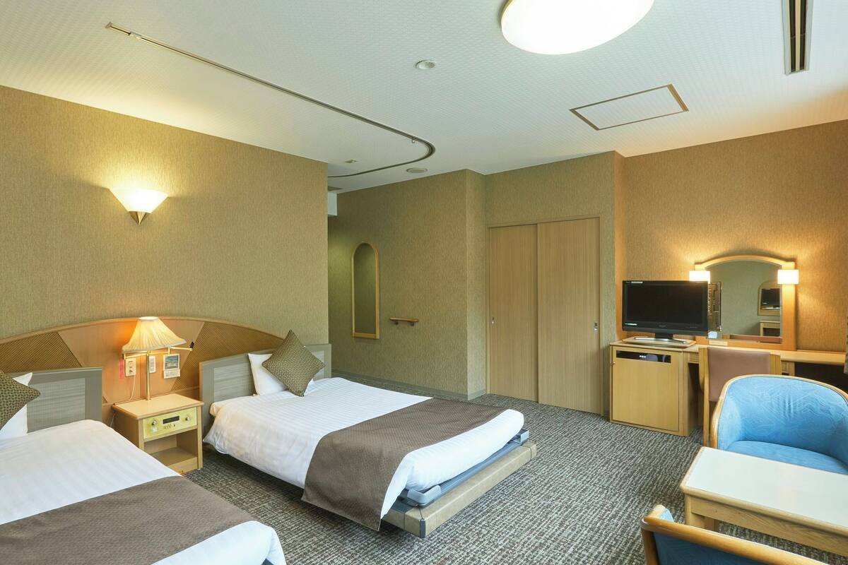 Une chambre d’hôtel avec deux lits, un bureau avec un ordinateur, une chaise, une télévision et un miroir.