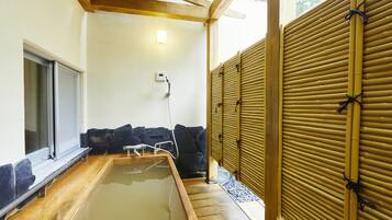 Un onsen japonés tradicional con una bañera de madera, un banco de piedra y una celosía de bambú.