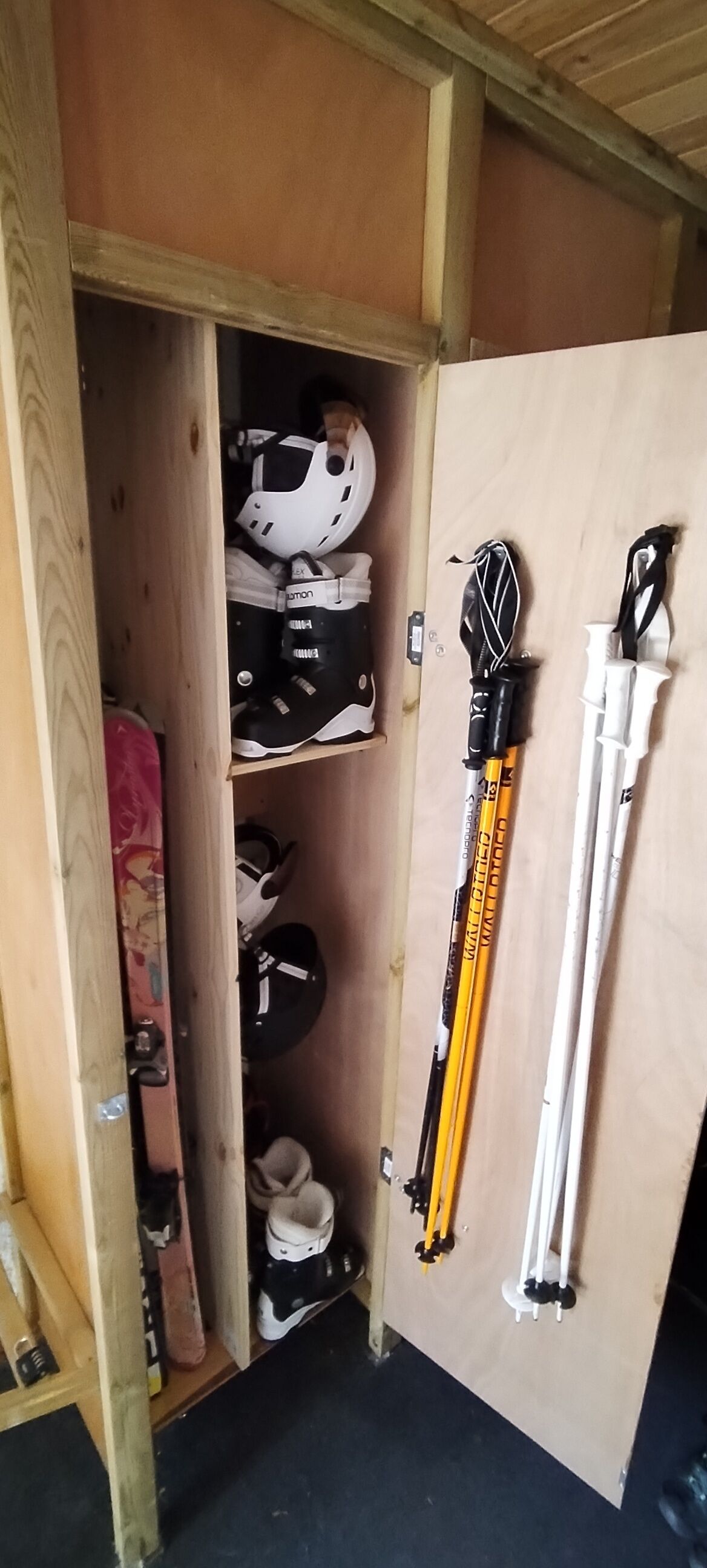 A wooden storage unit with skis and ski helmets.