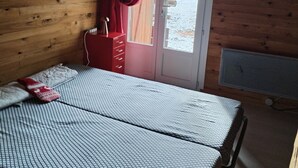 A wooden cabin room with a bed, a red dresser, a window with red curtains, and a view of a snowy landscape. - APARTMENT DUPLEX SUPER SAUZE 1700 (LE SUPER SAUZE, Enchastrayes)