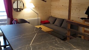 A modern living room with a wooden wall, a round mirror, a wooden coffee table, a grey sofa, and a red throw pillow. - APARTMENT DUPLEX SUPER SAUZE 1700 (LE SUPER SAUZE, Enchastrayes)