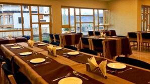 Un espace repas avec de longues tables disposées pour accueillir de nombreux convives, de grandes fenêtres offrant une vue agréable et un aménagement intérieur épuré et moderne.