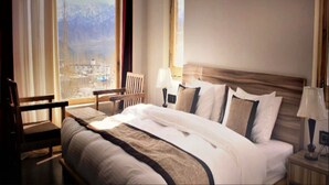 Une chambre d’hôtel avec un grand lit, une chaise, une table de chevet et une vue sur les montagnes par la fenêtre.