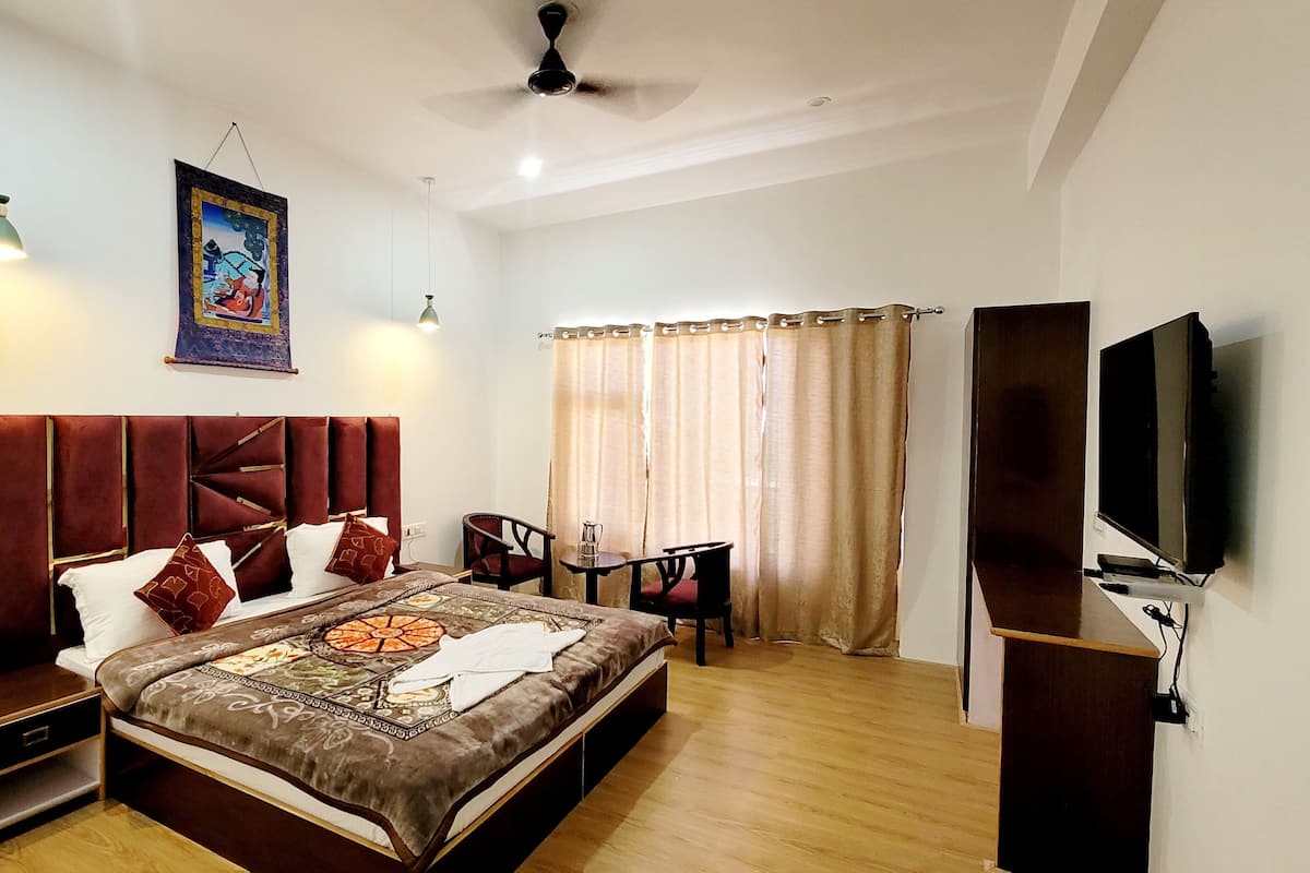 Une chambre à coucher avec un grand lit, une télévision, un ventilateur de plafond et une fenêtre avec des rideaux.