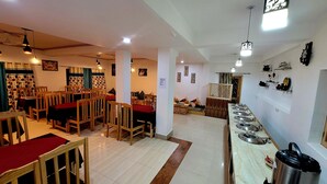 Un restaurante con mesas y sillas de madera, una barra de buffet con platos, y un letrero que indica servicio de zumos y desayuno.