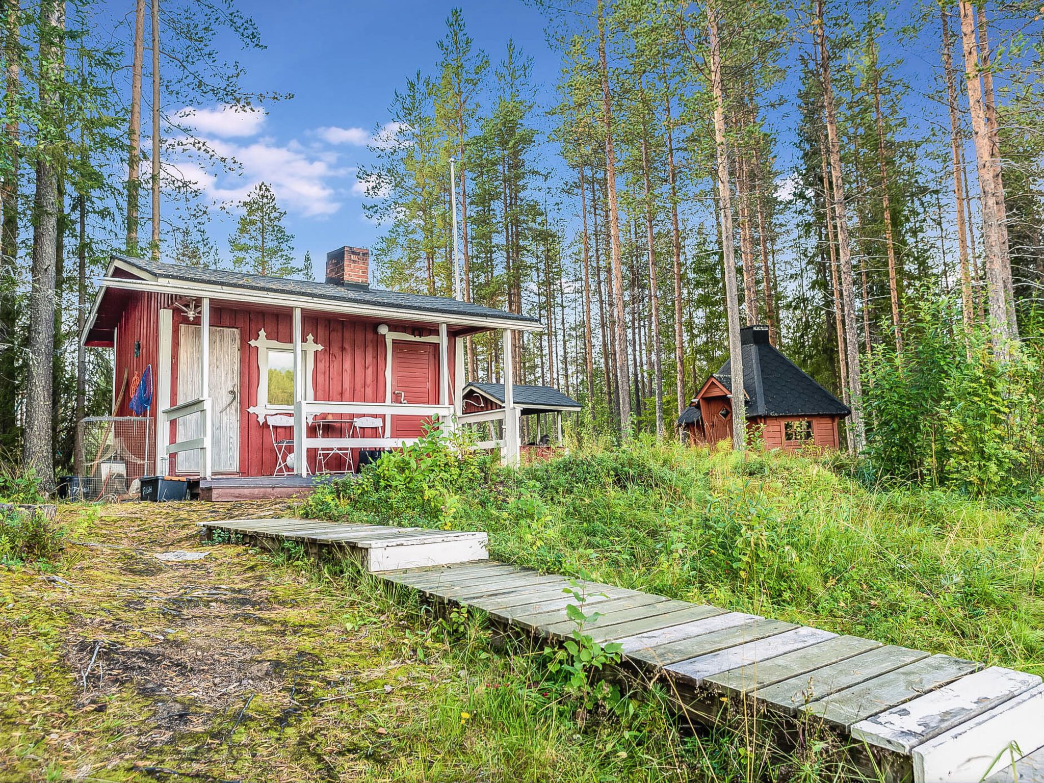 Eine Hütte mit roter Fassade, einer kleinen Veranda und einem Holzsteg, der zu ihr führt.