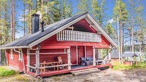 Punainen mökki, jossa on kuisti, savupiippu ja pieni terassi.