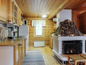 Puinen sisustus, jossa on keittiöalue, kivinen takka ja ikkuna, jossa on verhot.