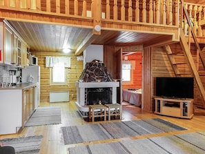 A cozy cabin interior with a kitchen, a fireplace, a television, and a staircase.