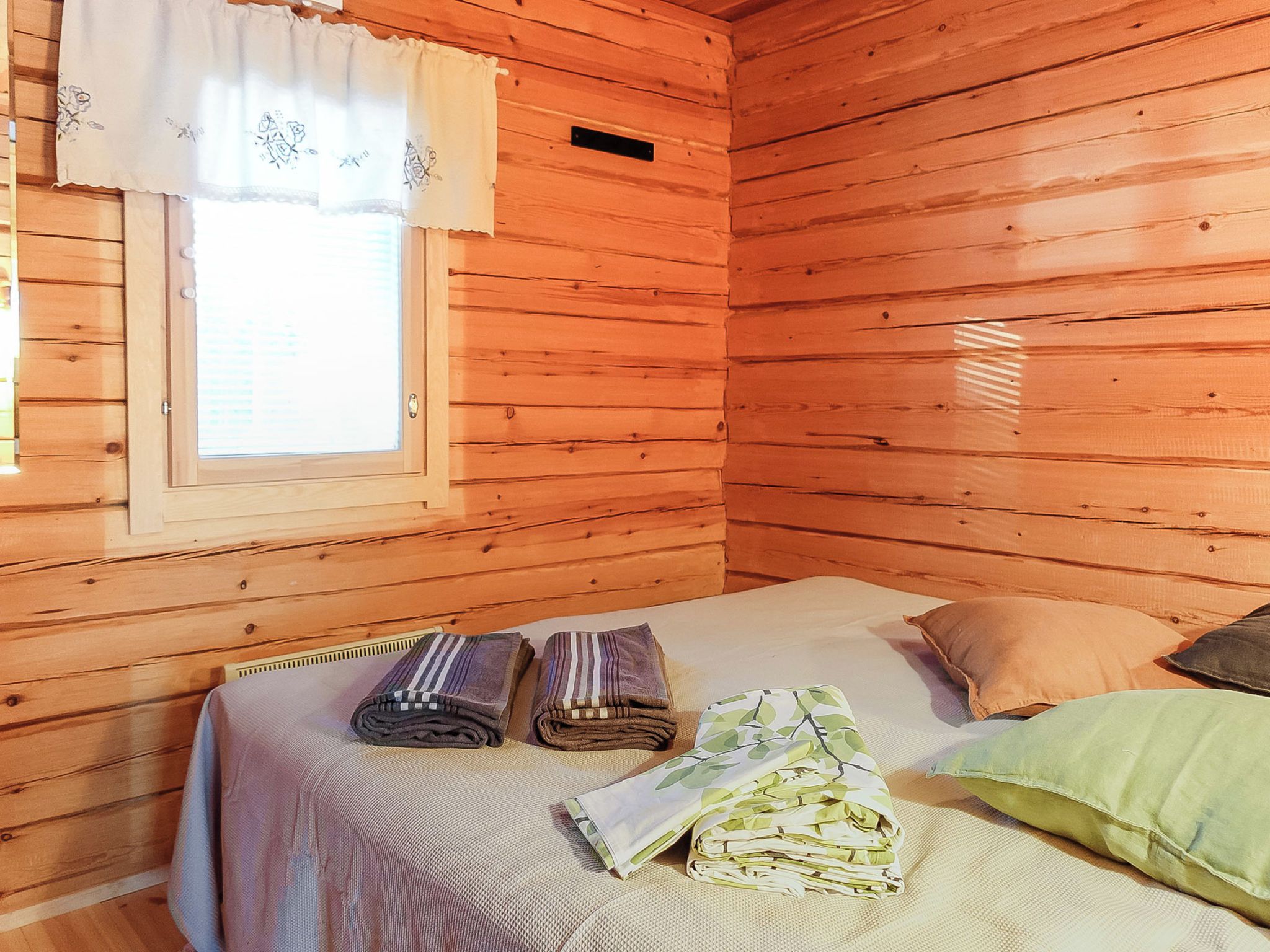 Een houten kamer met een bed, kussens en een raam met gordijnen.