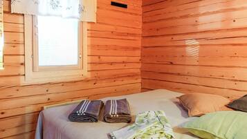Een houten kamer met een bed, kussens en een raam met gordijnen.