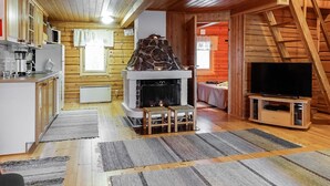 Tunnelmallinen mökin sisustus, jossa on kivinen takka, puinen portaikko ja televisio puukehikossa.