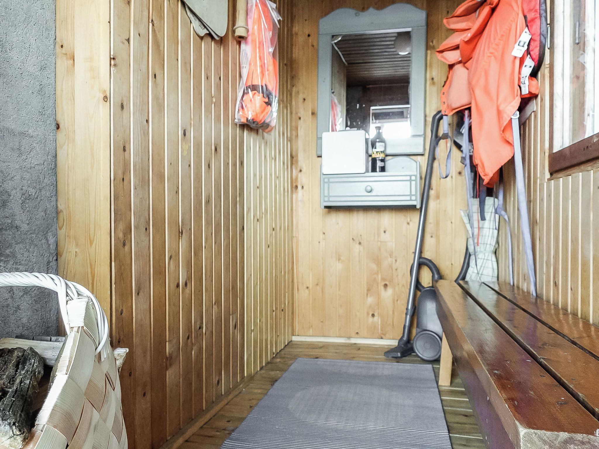 Un couloir étroit aux murs en bois, un petit banc et un aspirateur.