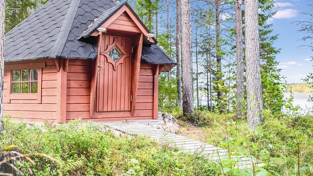 Pieni puinen mökki, jossa on jyrkkästi kallistuva katto, savupiippu ja koristeellinen ovi.