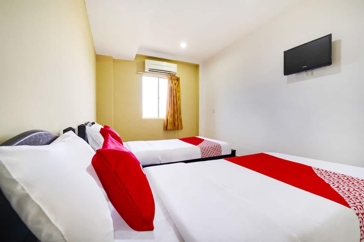 Ein Hotelzimmer mit zwei Betten, einem an der Wand befestigten Fernseher und einer Klimaanlage über einem Fenster.