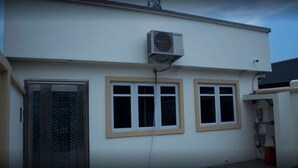 A building with a white exterior, a metal door with a glass panel, and two windows with beige frames. - Craven Cottage Inn (Lagos)