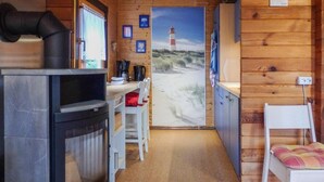 Interior acolhedor de uma cabana com lareira a lenha, área de jantar e vista para uma praia com um farol.