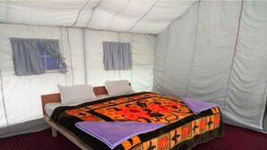 Cama de casal com colcha floral e manta roxa em um quarto tipo tenda com carpete vermelho.
