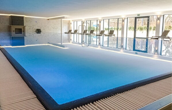 Une piscine intérieure avec des parois en verre transparent, un sol carrelé et quelques chaises longues.