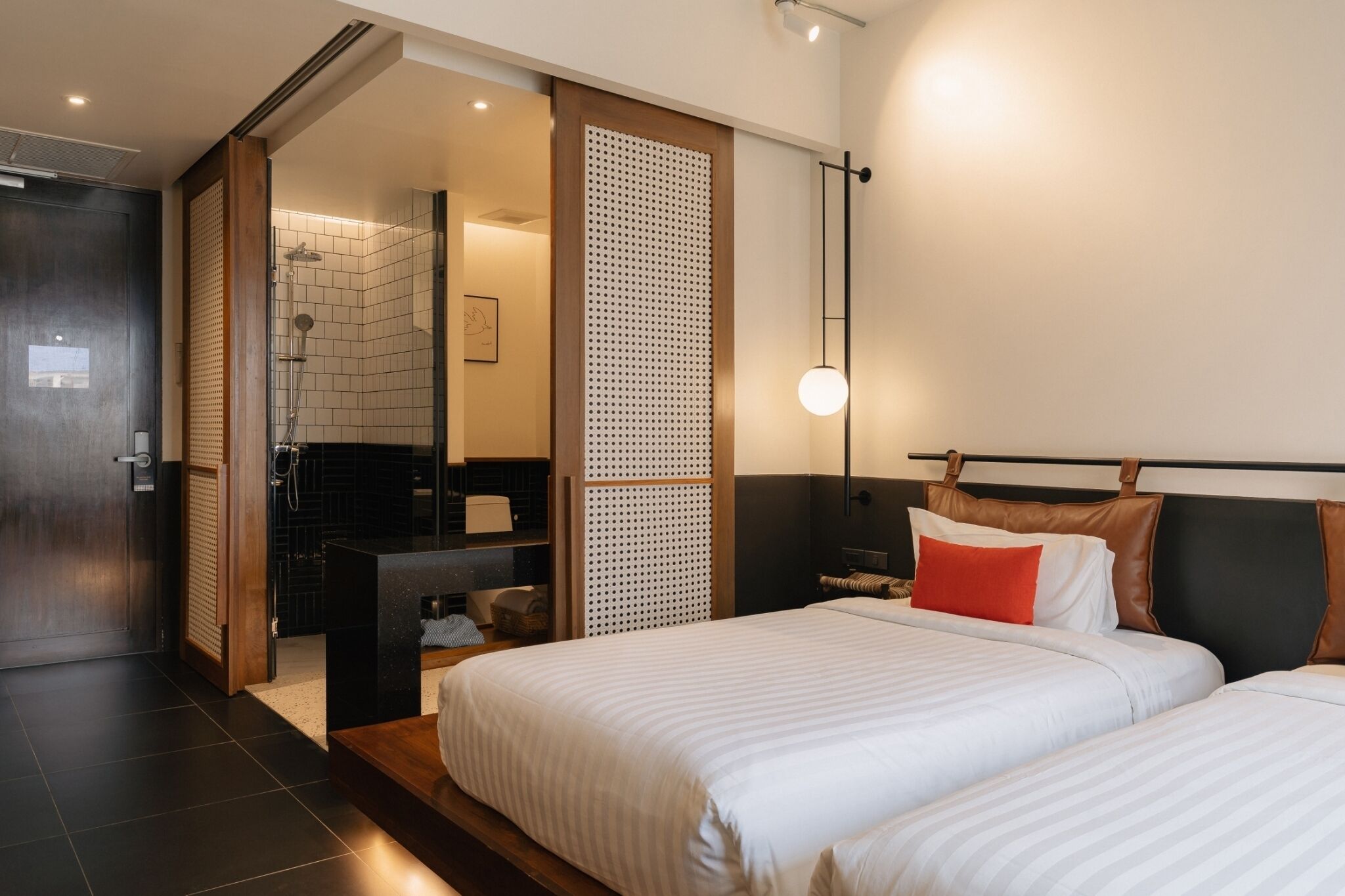 A modern hotel room with two beds, a bathroom with a shower, and a large window.