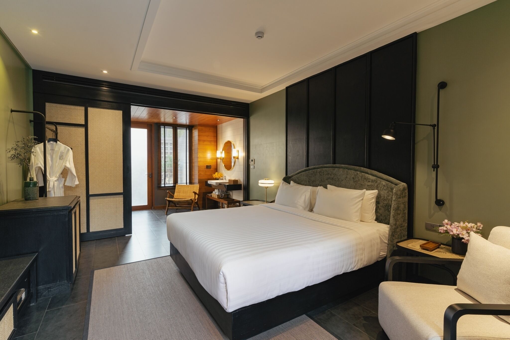 A modern hotel room with a large bed, a desk, a chair, and a small table with a lamp.