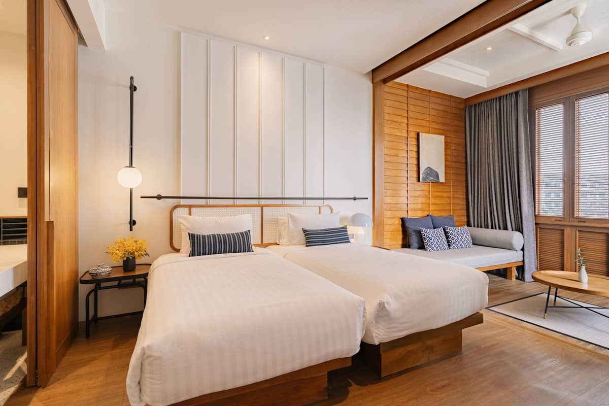 Une chambre d’hôtel moderne avec deux lits, un canapé, une petite table et une grande fenêtre avec des rideaux.