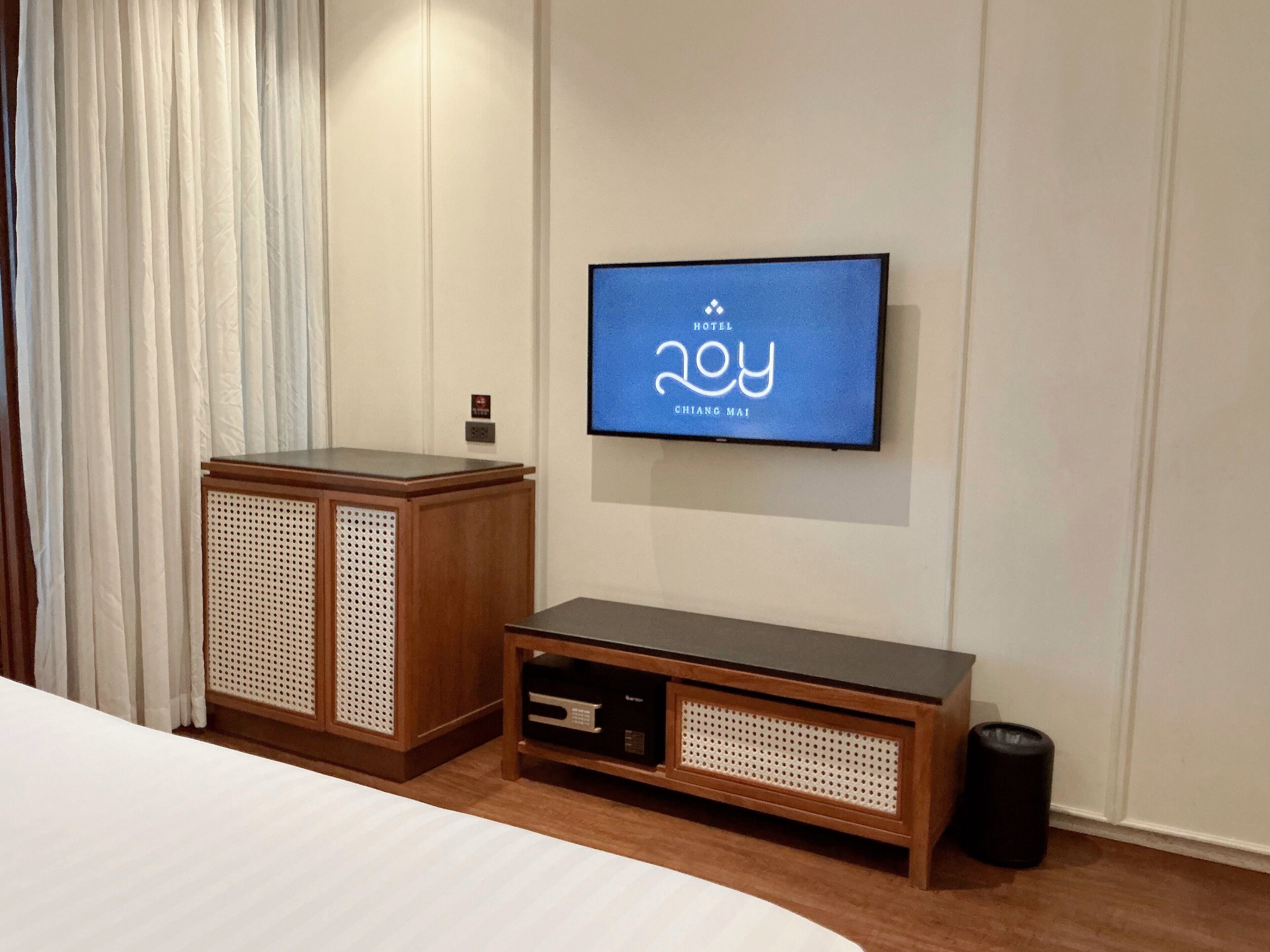 A hotel room with a bed, a TV mounted on the wall, a wooden cabinet, and a trash can.