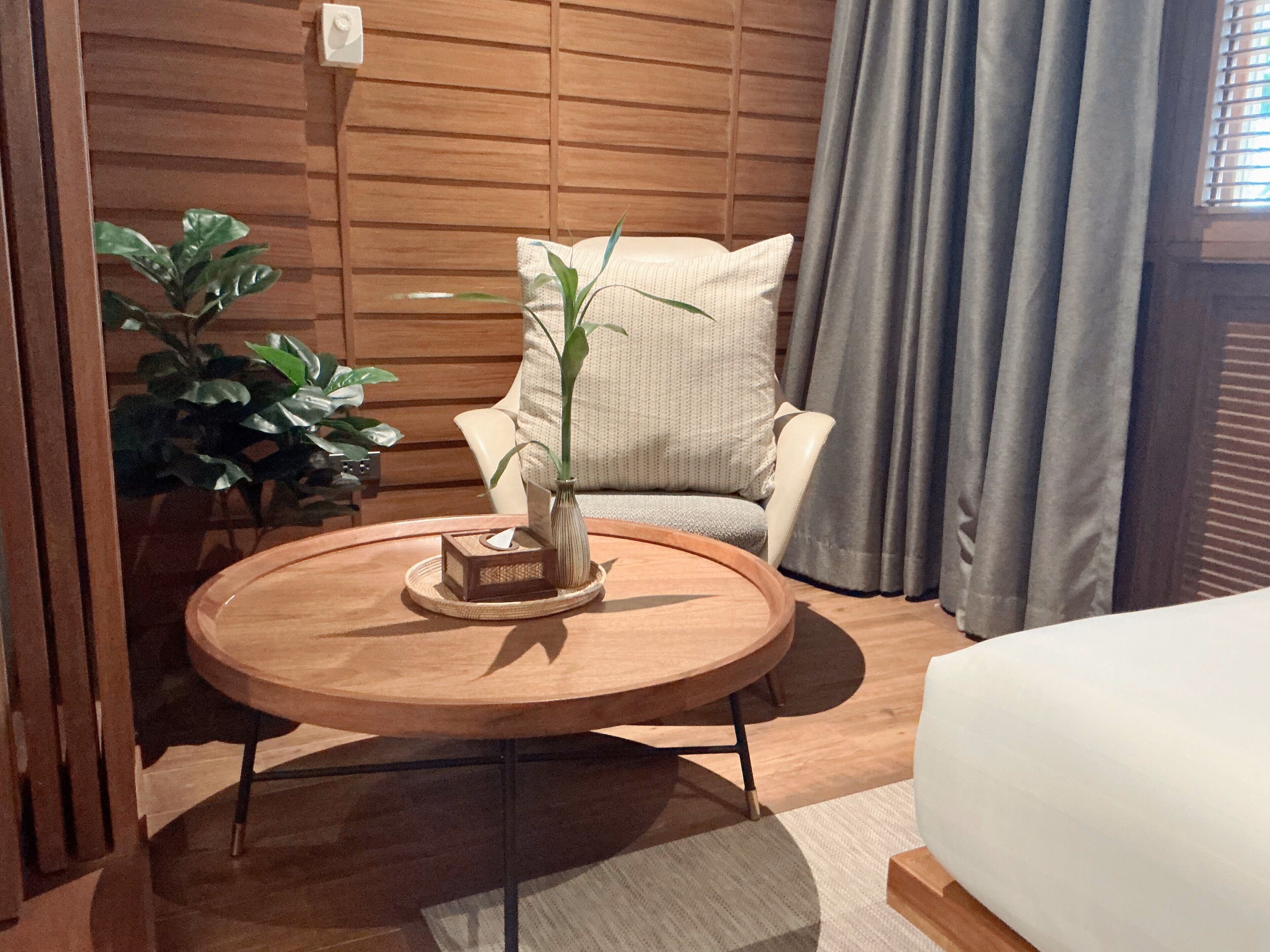 Une pièce avec une table ronde en bois, une plante en pot, un canapé et une fenêtre avec des rideaux.