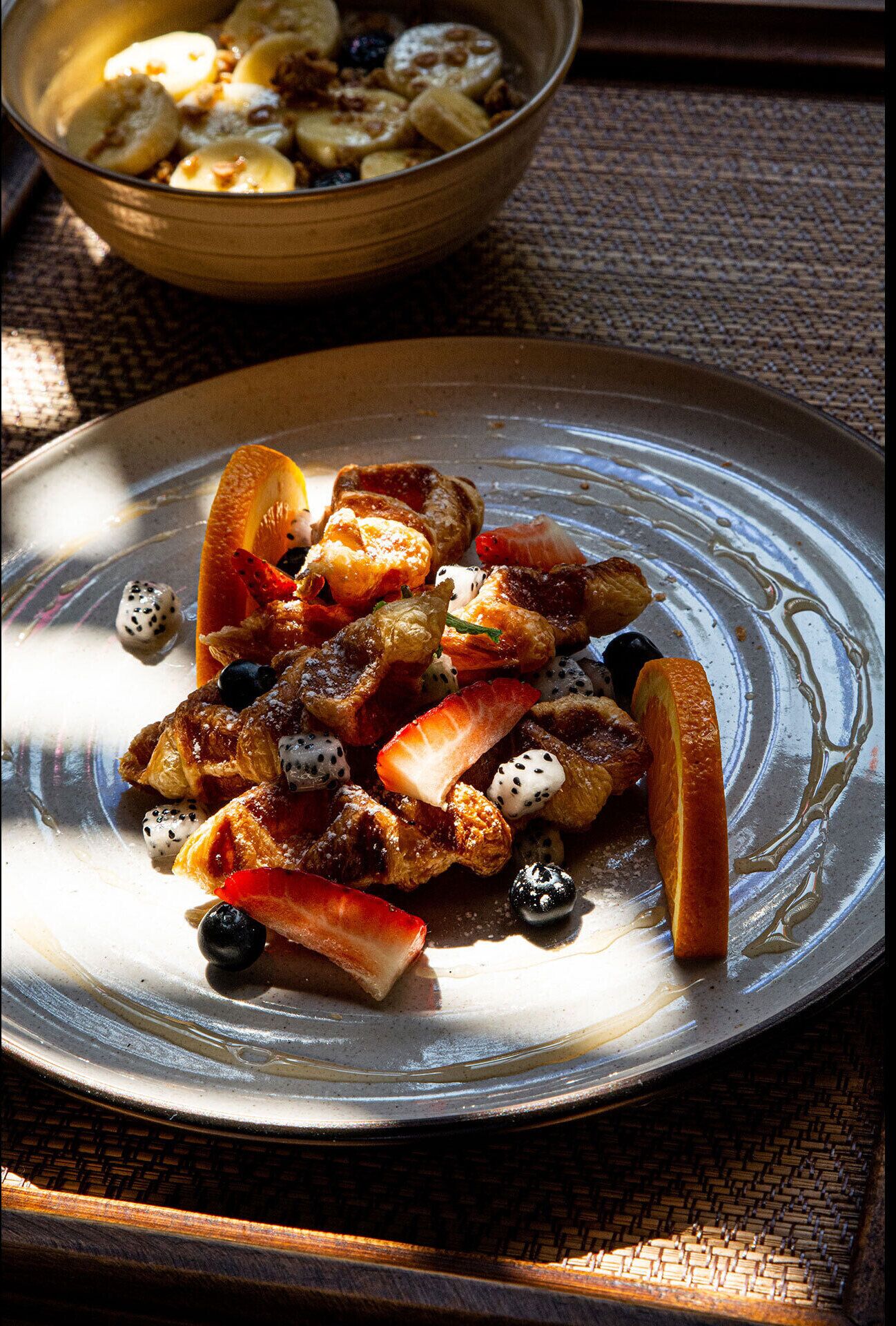A plate of food with various fruits and nuts, and a bowl of similar food in the background.