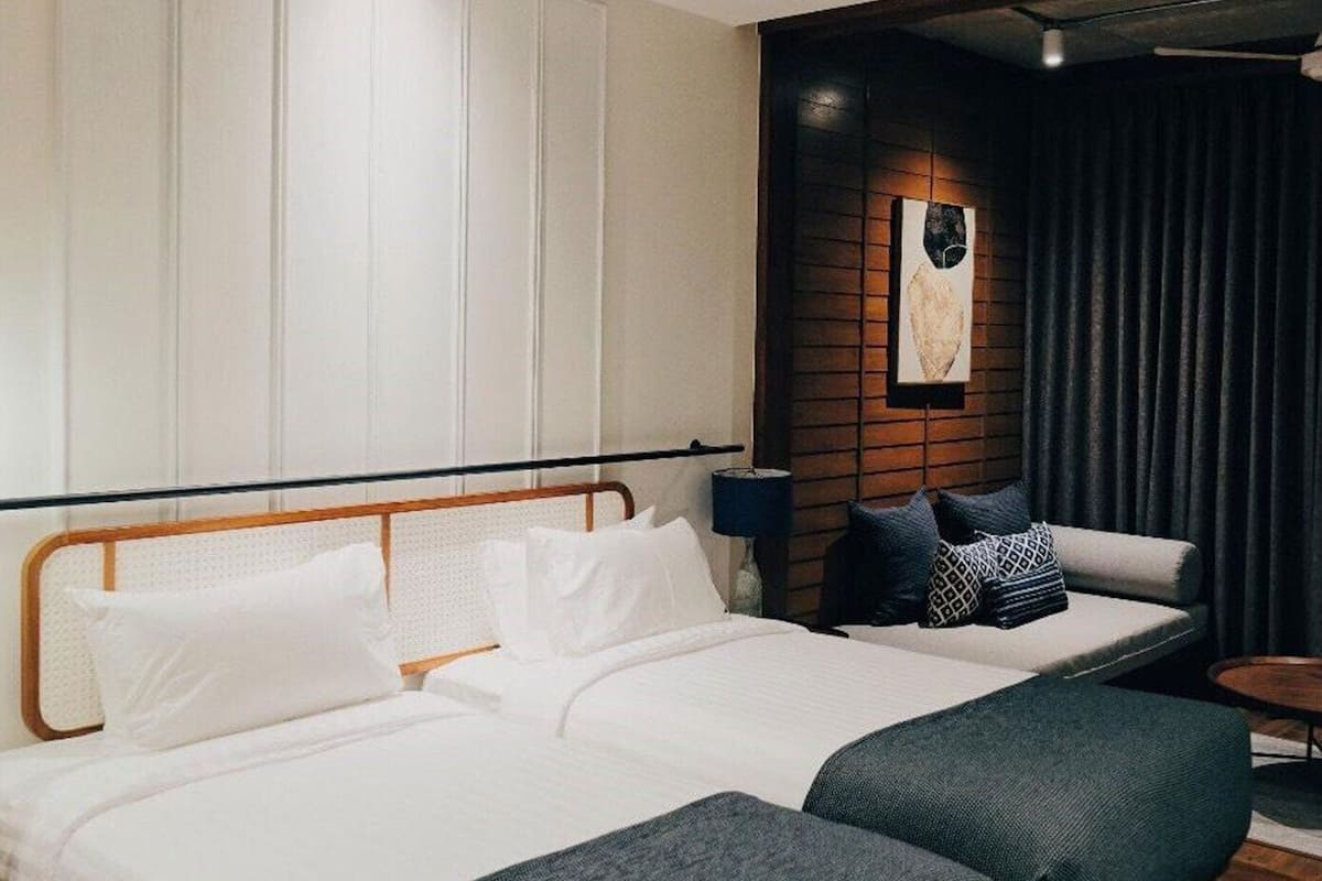 Une chambre d’hôtel moderne avec un grand lit, deux tables de chevet, un rideau foncé et une œuvre d’art accrochée au mur.