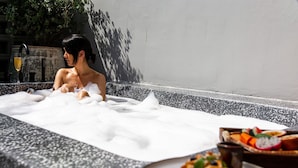 Une personne se détend dans un bain à remous rempli de bulles, avec une assiette de fruits et une boisson à proximité.