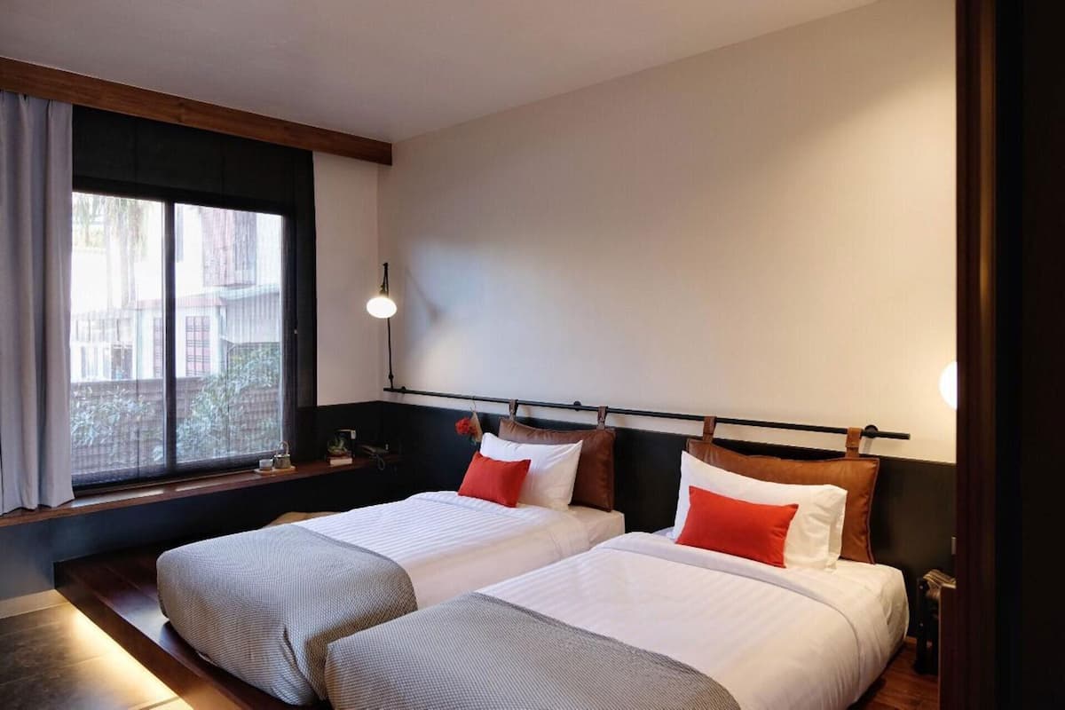 Une chambre d’hôtel avec deux lits, une fenêtre avec des rideaux, une table de chevet et une lampe.