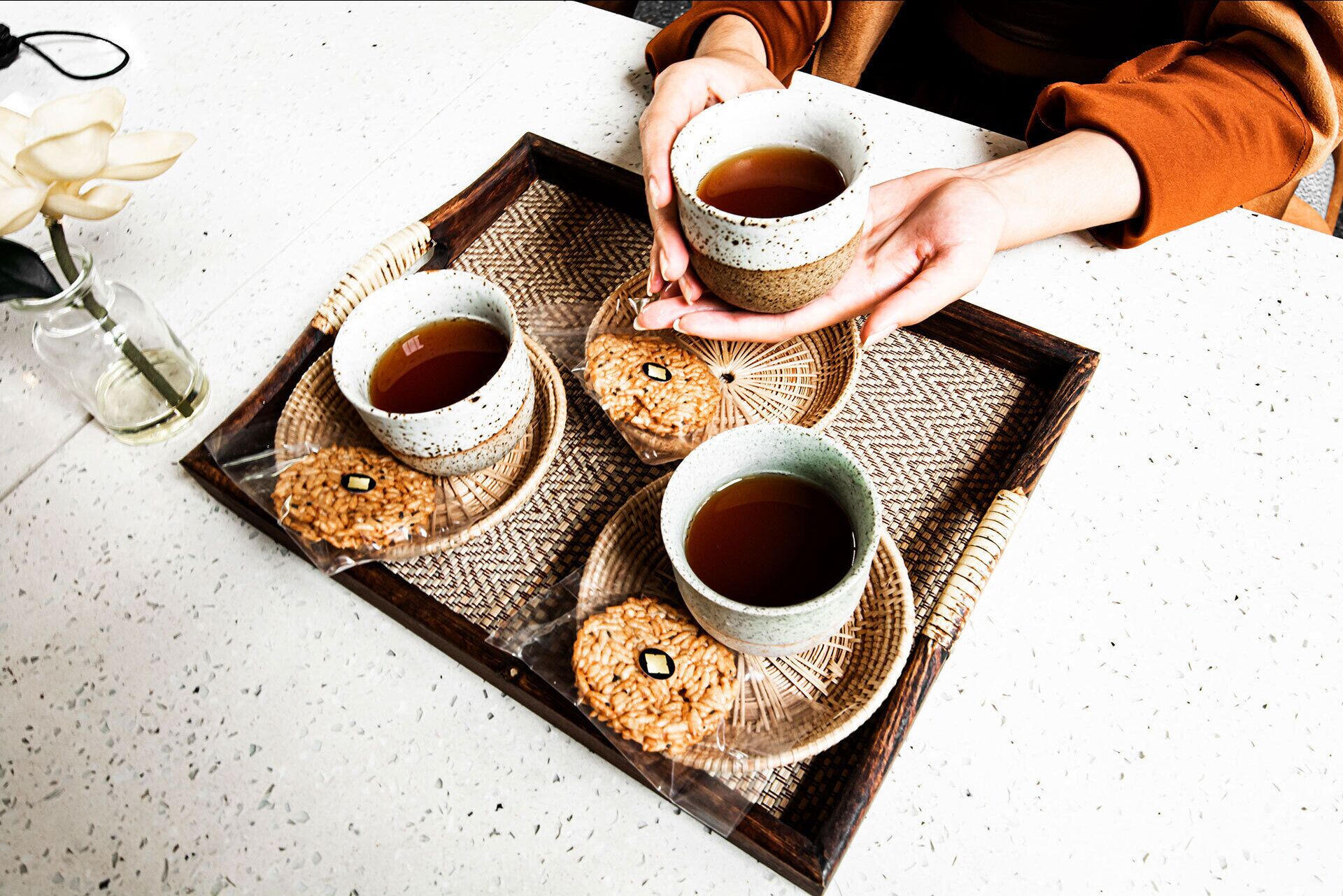 A tray with four cups of tea and two cookies on a white surface.