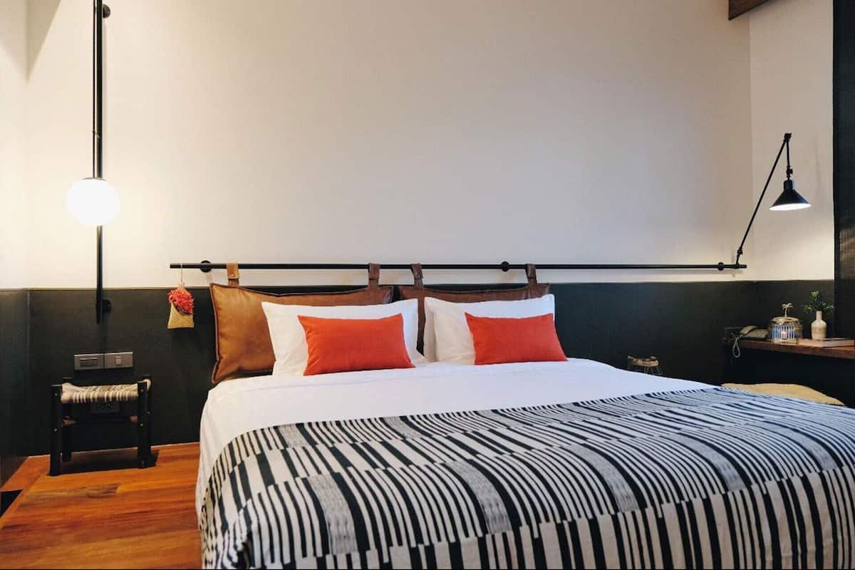 Un lit bien fait, avec une couvre-lit à rayures, une tête de lit ornée de coussins en cuir et une lampe de chevet.