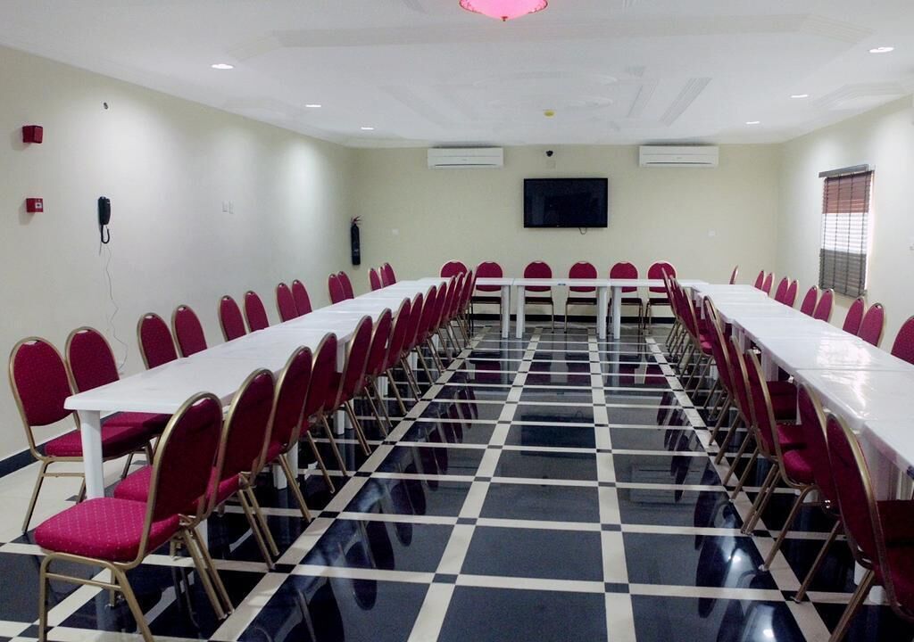 Ein Konferenzraum mit langem Tisch und roten Stühlen, weißen Wänden und einem karierten Boden.